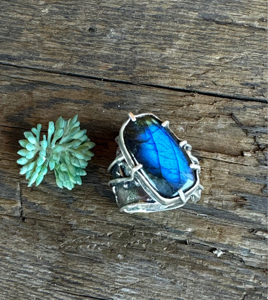 A sterling silver ring with a blue flash labradorite stone set in a rectangular shape, attached to a textured band.