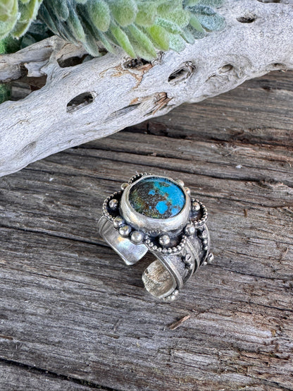 Desert Flower Turquoise & Silver ring with a central gemstone on a wooden surface with natural elements.